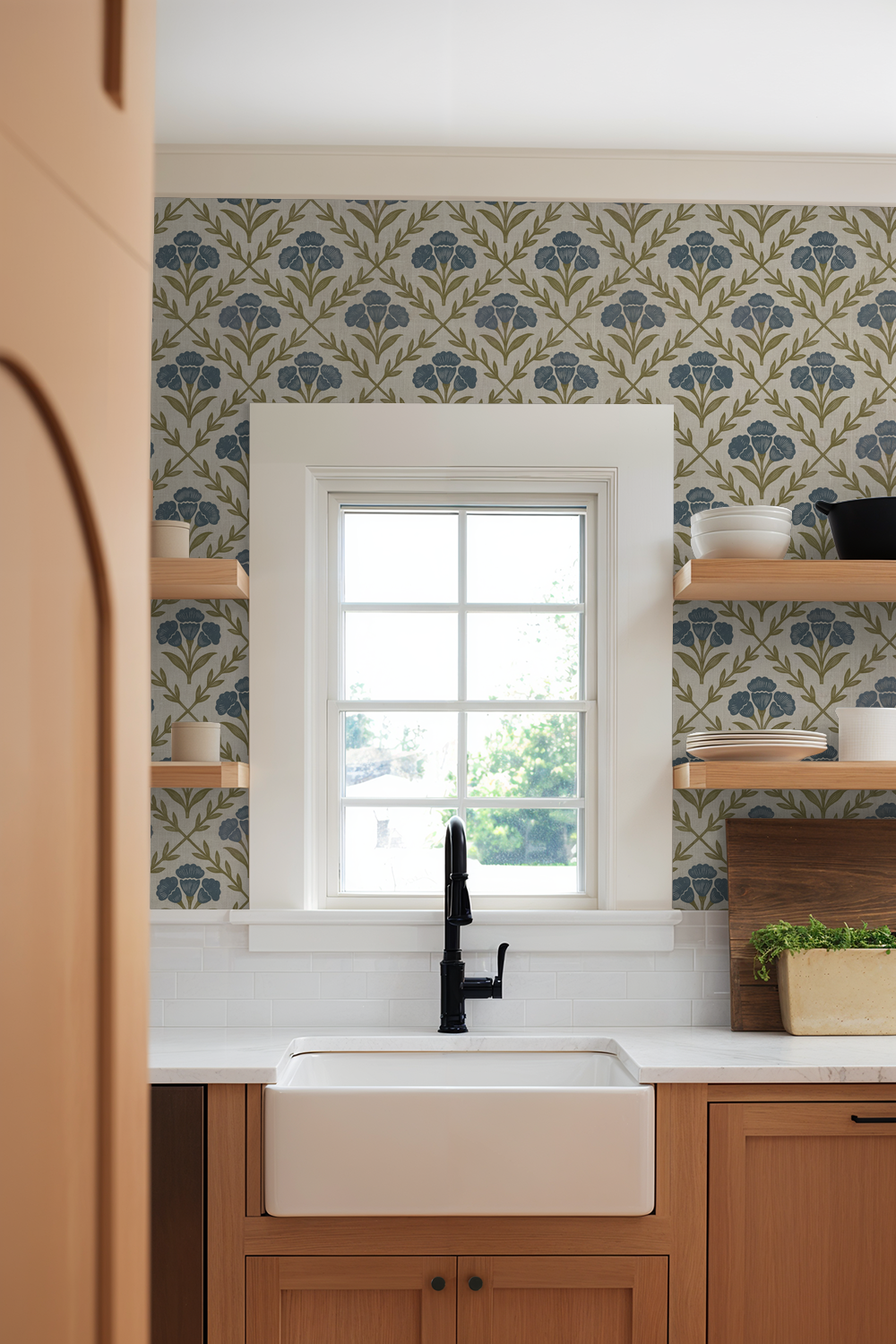 Kitchen with blue and olive floral wallpaper, white sink, wooden shelves