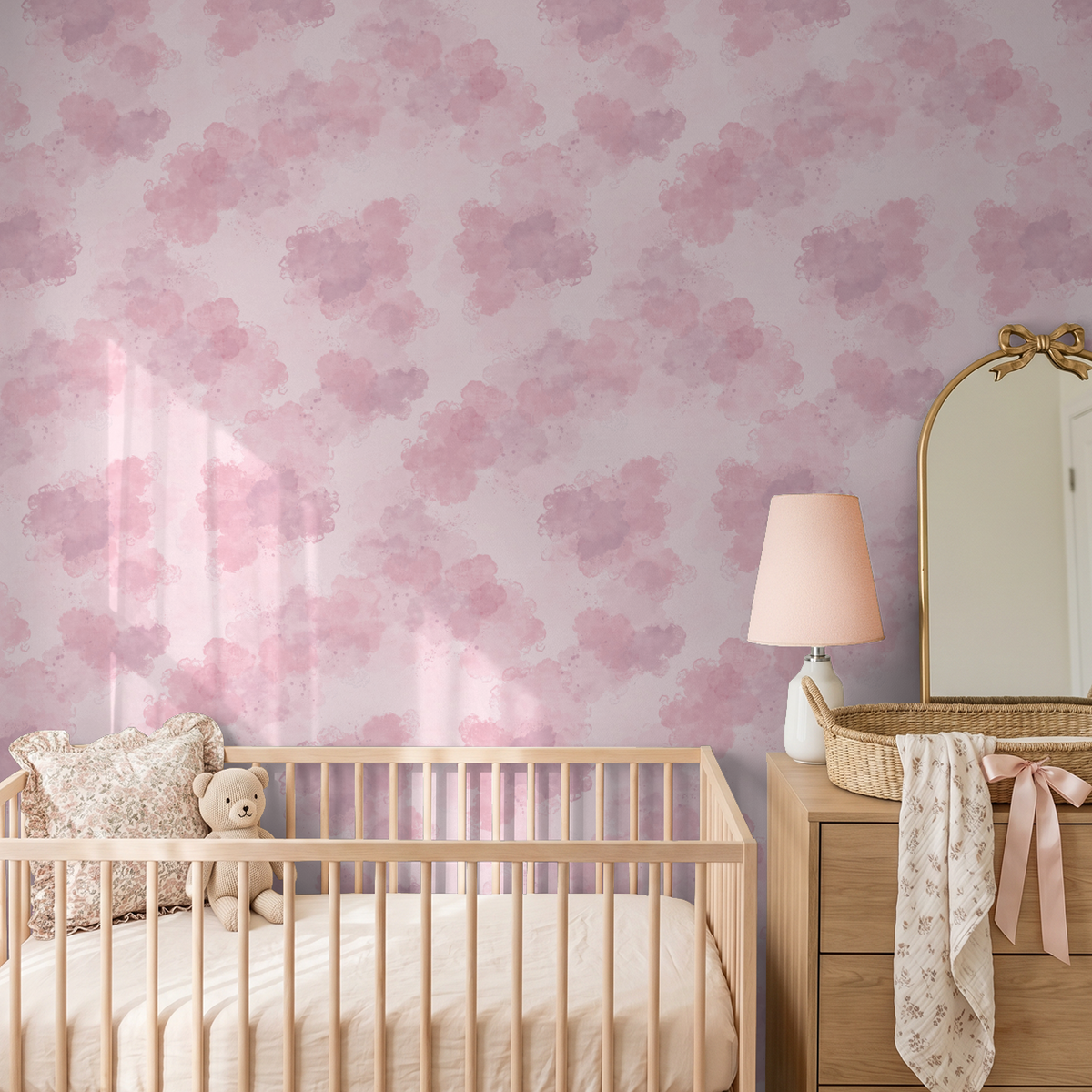 Blush pink watercolor cloud wallpaper in a serene nursery setting with crib and lamp.