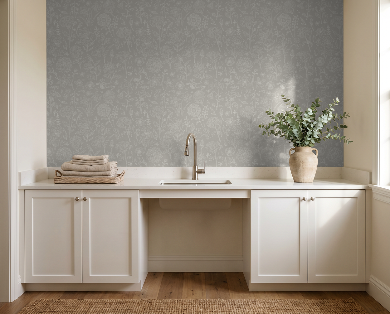 Gray floral outline wallpaper in a minimalist laundry room with white cabinets and a beige vase.