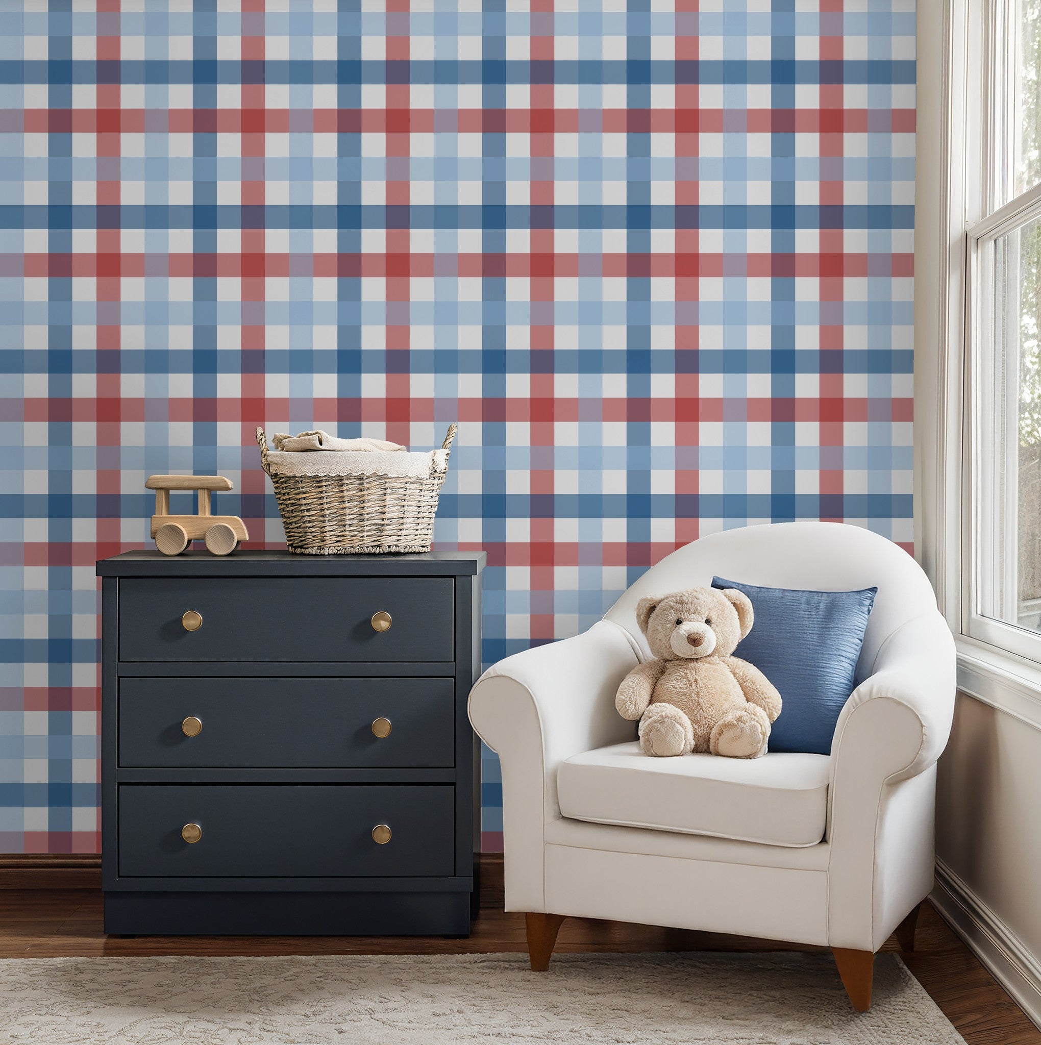 Red and blue gingham wallpaper in cozy nursery with white armchair and dark dresser.