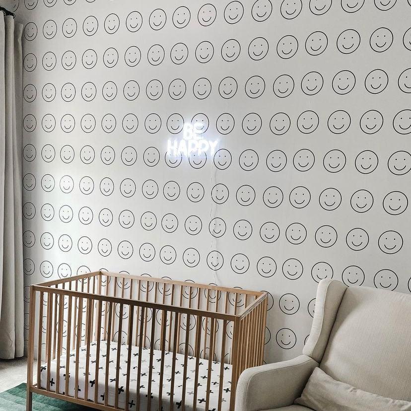 Wall Blush SG02 Be Happy Wallpaper in a cozy nursery room, with wooden crib and armchair.