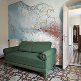 "Montage Wallpaper by Wall Blush accenting living room wall behind a green sofa, patterned tile flooring in view."