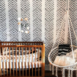 "Ar-row Wallpaper by Wall Blush in a stylish nursery room, featuring crib and hanging chair with wallpaper as focus."