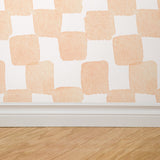 "Peachy Plaid Wallpaper by Wall Blush in a modern room, focusing on the wall decor with wooden flooring detail."