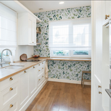 "Wall Blush Green Valley Wallpaper accent in modern kitchen, with white cabinets and wooden floor."