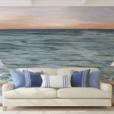 "Wall Blush New Beginnings Wallpaper in cozy living room, ocean-inspired design behind beige couch with blue pillows."