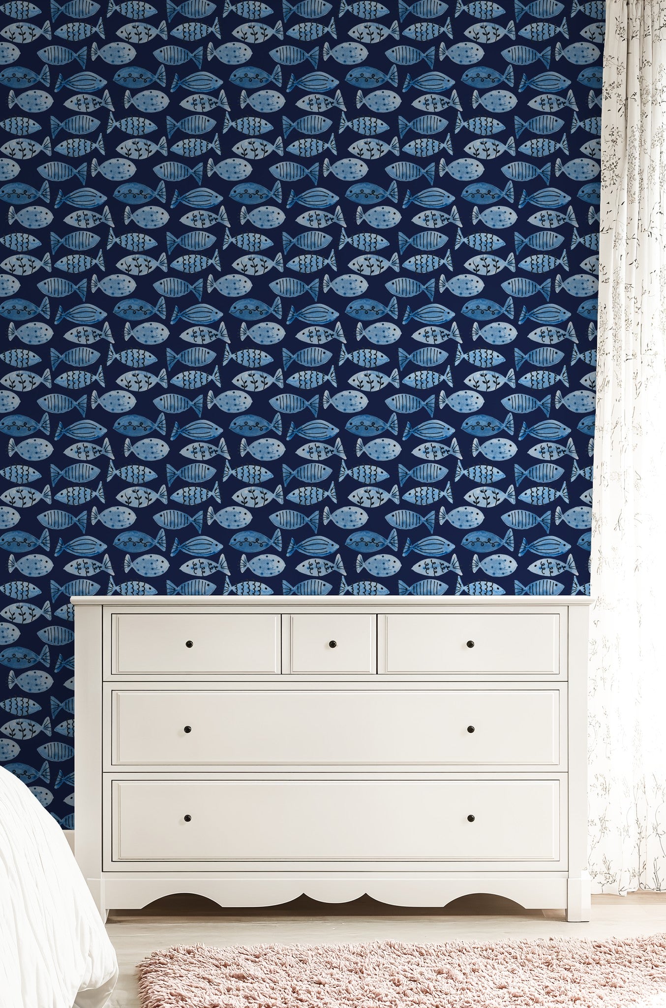 Blue fish pattern wallpaper in a bedroom with white dresser and pink rug.