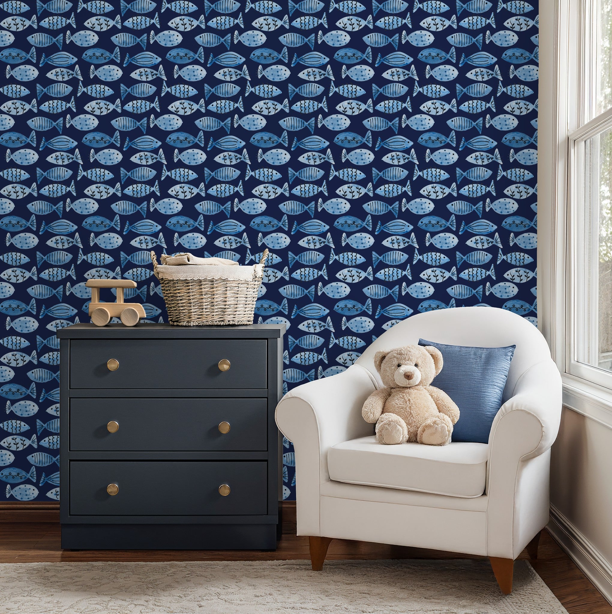 Blue fish pattern wallpaper in cozy child's room with navy dresser and white armchair.