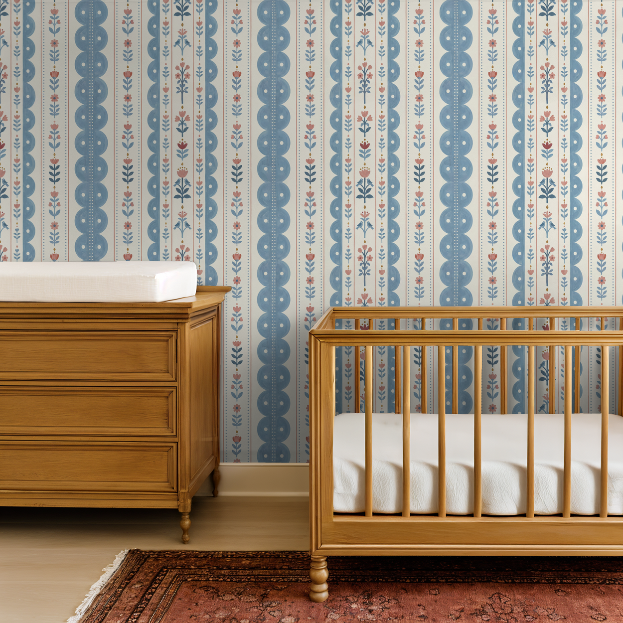 Dahlia Dreams wallpaper with blue and coral floral stripes in a nursery with wooden crib and dresser.