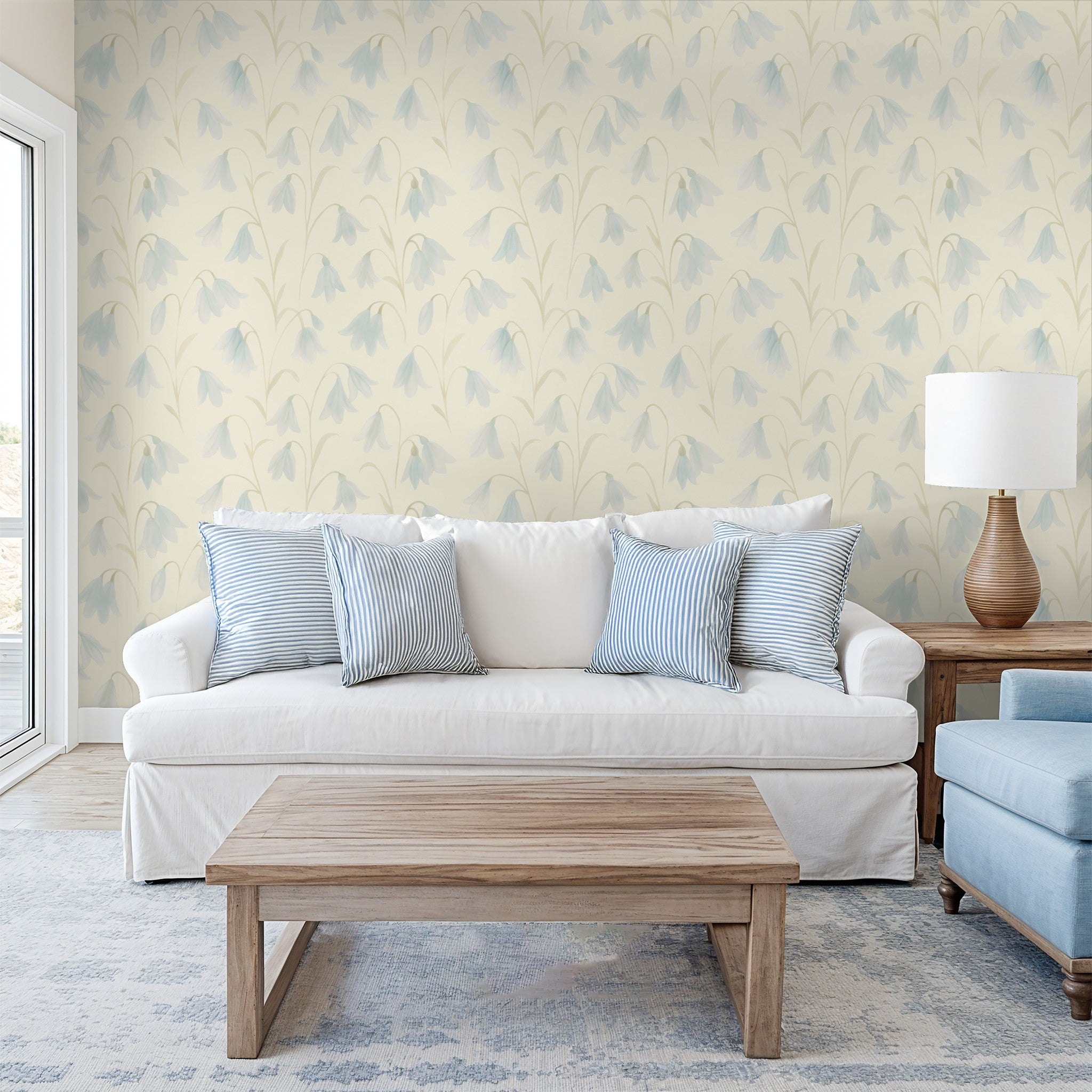 Floral blue and cream wallpaper in a sunlit living room with white sofa and wooden furniture.
