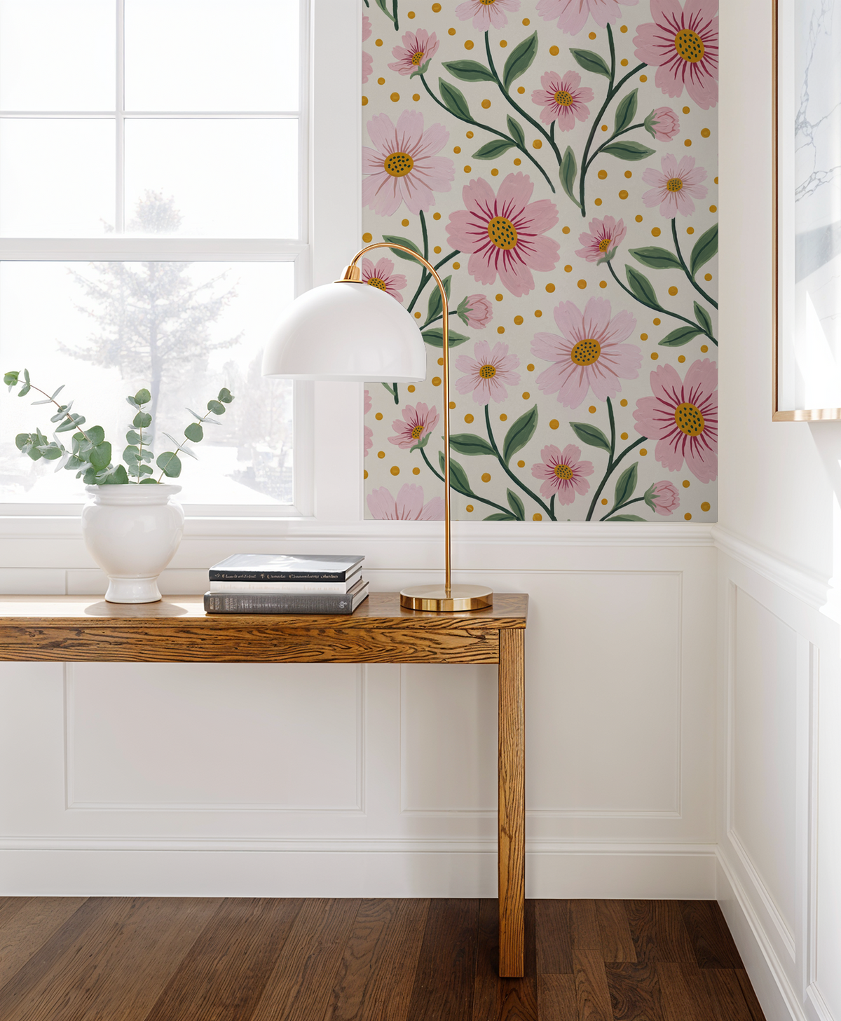 Pink floral wallpaper with green leaves in a bright room with wooden table and lamp.