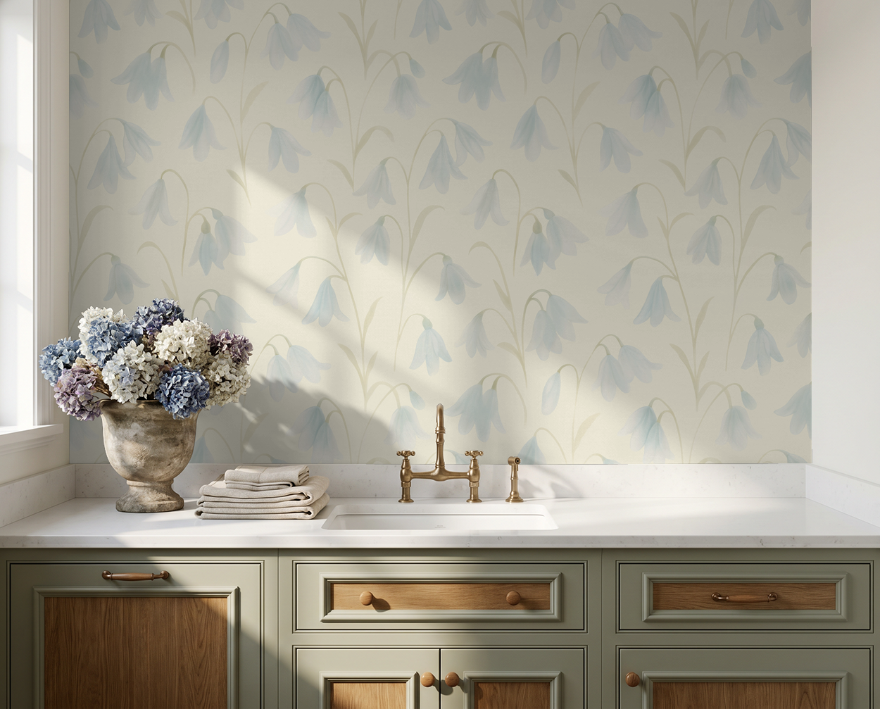 Soft blue floral wallpaper in a sunlit kitchen with green cabinets and hydrangeas.
