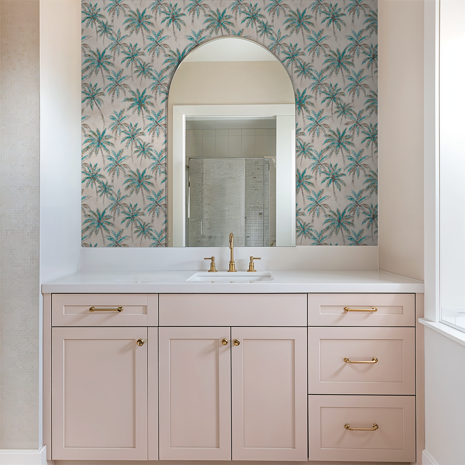 Tropical palm tree wallpaper in bathroom with pink vanity and gold fixtures.